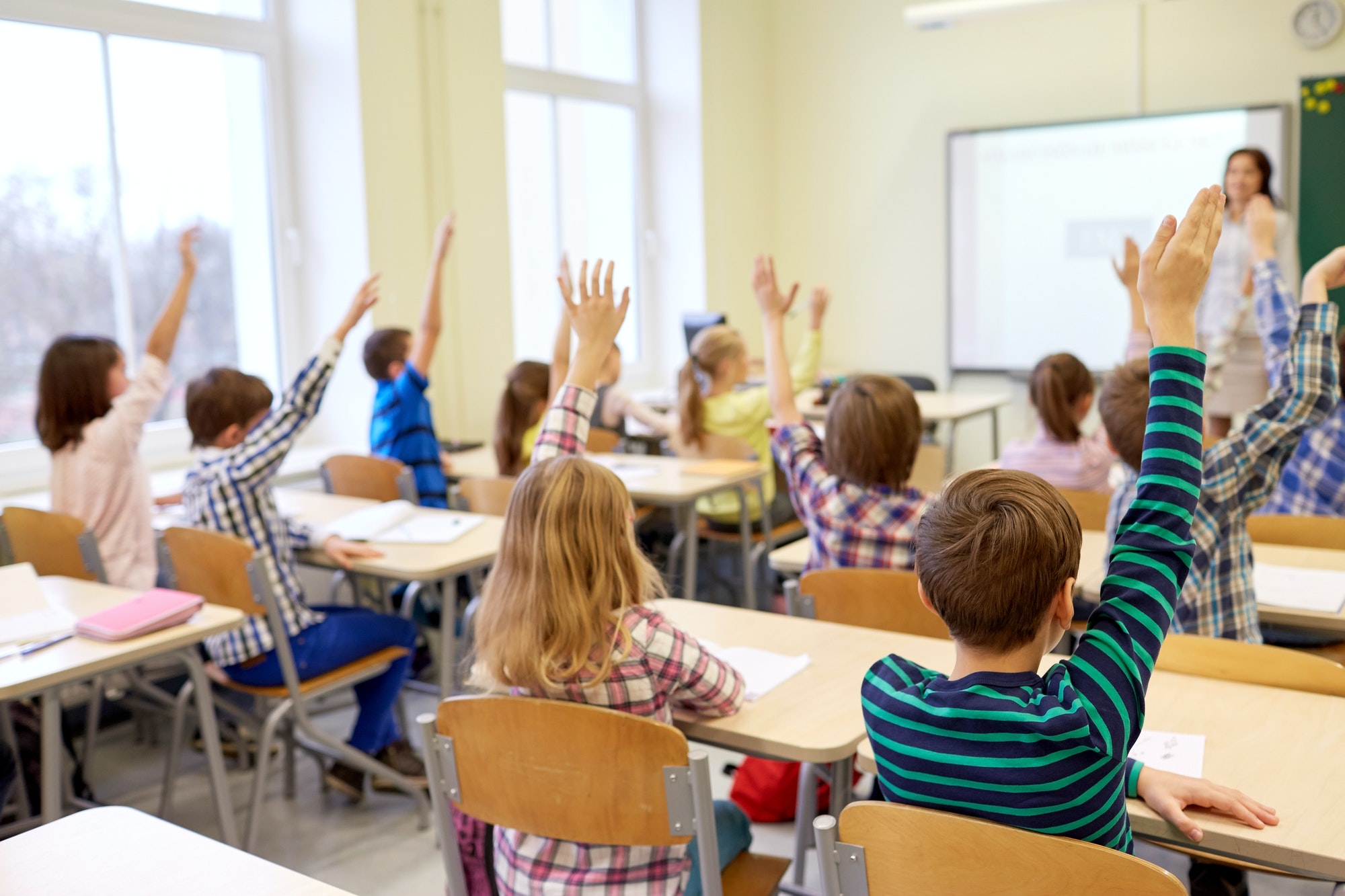 group-of-school-kids-raising-hands-in-classroom
